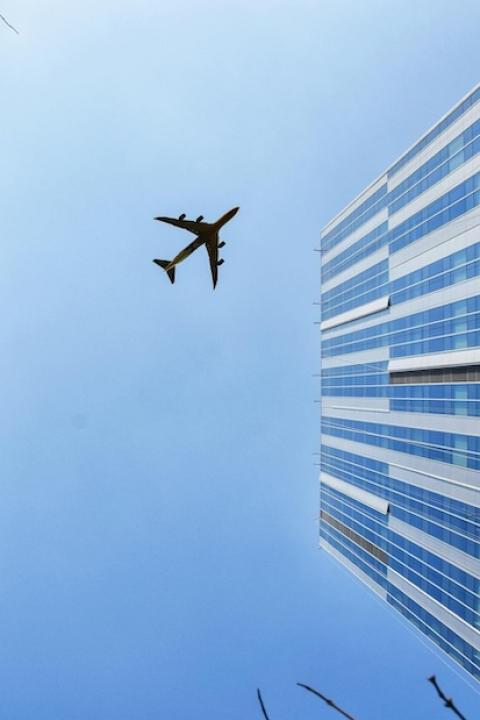 Airplane flying in the sky above two buildings — sustainable aviation fuels copy