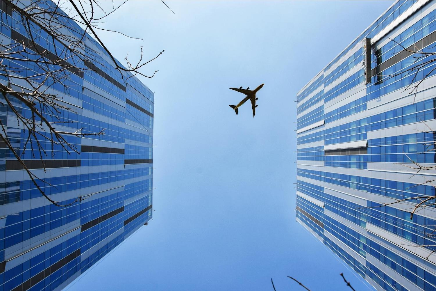 Airplane flying in the sky above two buildings — sustainable aviation fuels copy