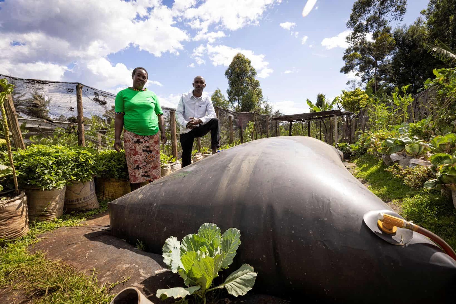 Two farmers stand next to their Sistema.bio biodigester on their farm in Africa.