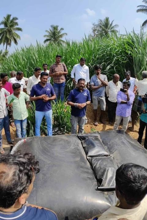 Farmers stand around a Sistema.bio biodigester on the ground that resembles and inflated black bag.