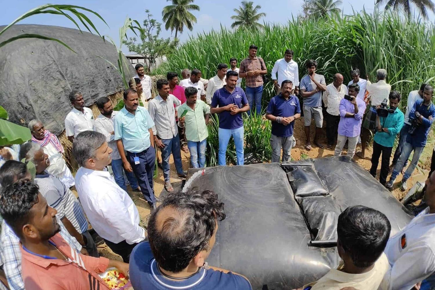 Farmers stand around a Sistema.bio biodigester on the ground that resembles and inflated black bag.