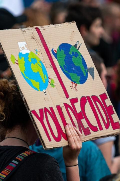 A climate activist holding a sign that reads, "You decide" — climate philanthropists