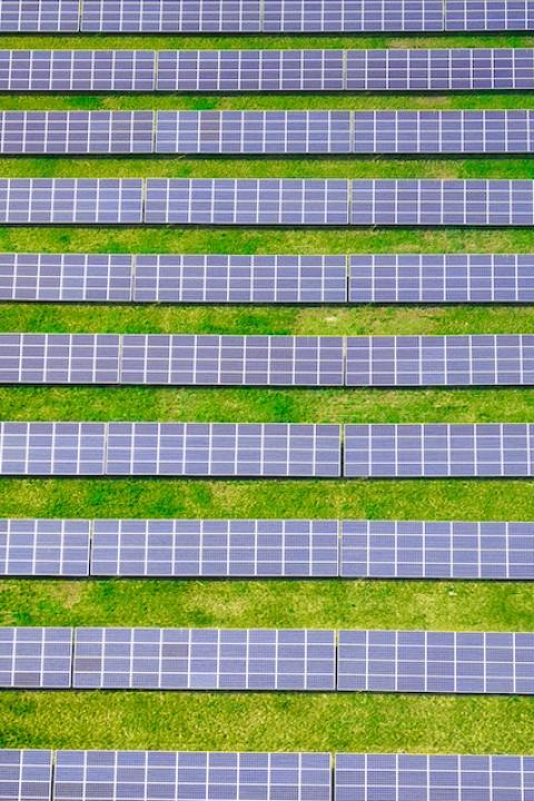 A birds eye view of lines of solar panels in a grass field — community solar