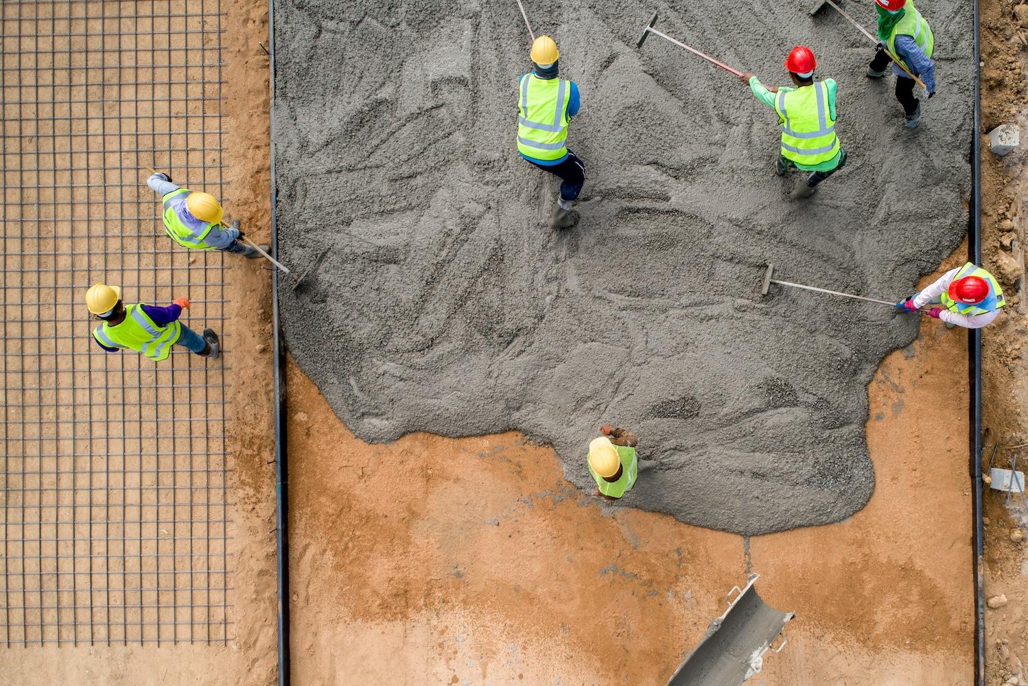 construction workers pour wet concrete at a road construction site — US businesses move toward low-carbon concrete
