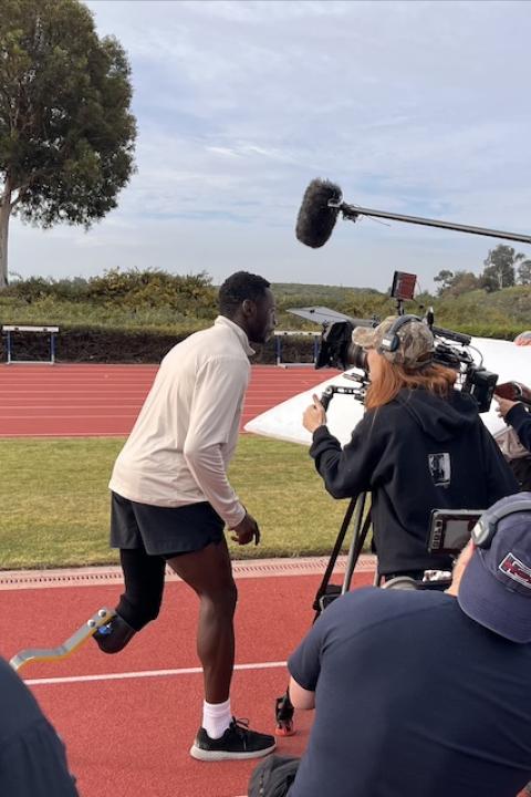 A crew films a public service announcement on a running track with Paralympic medalist Derek Loccident for the Creative Impact Lab.