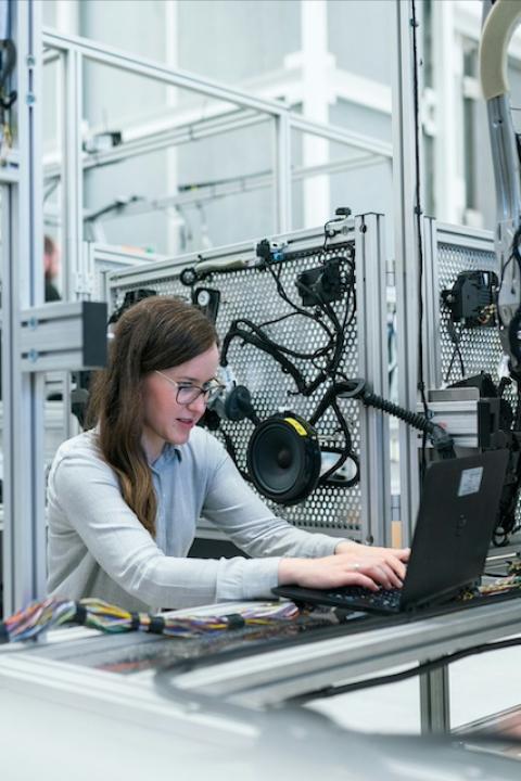 A woman works on a laptop in a factory — DEI