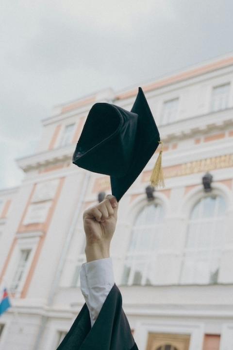 A person holding a graduation cap in the air — Excel Center