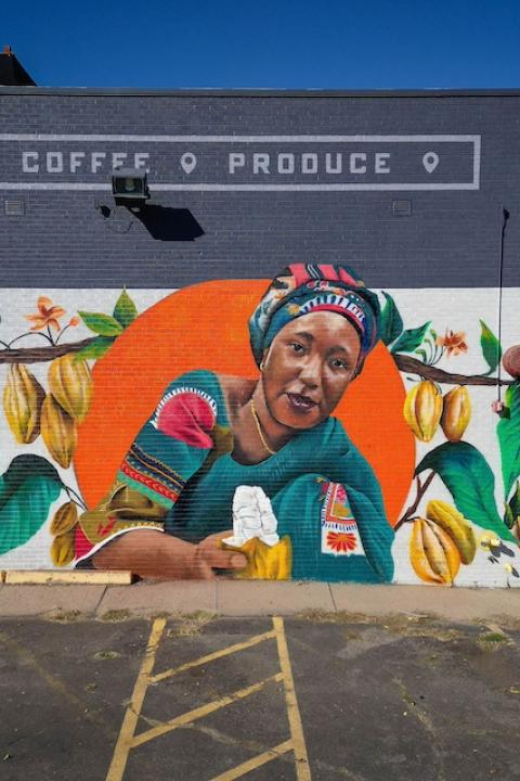 The mural depicting Salamatu Katta in an orange circle surrounded by a cacao tree on the wall of Leevers Locavore in Denver, Colorado — Fairtrade farmers