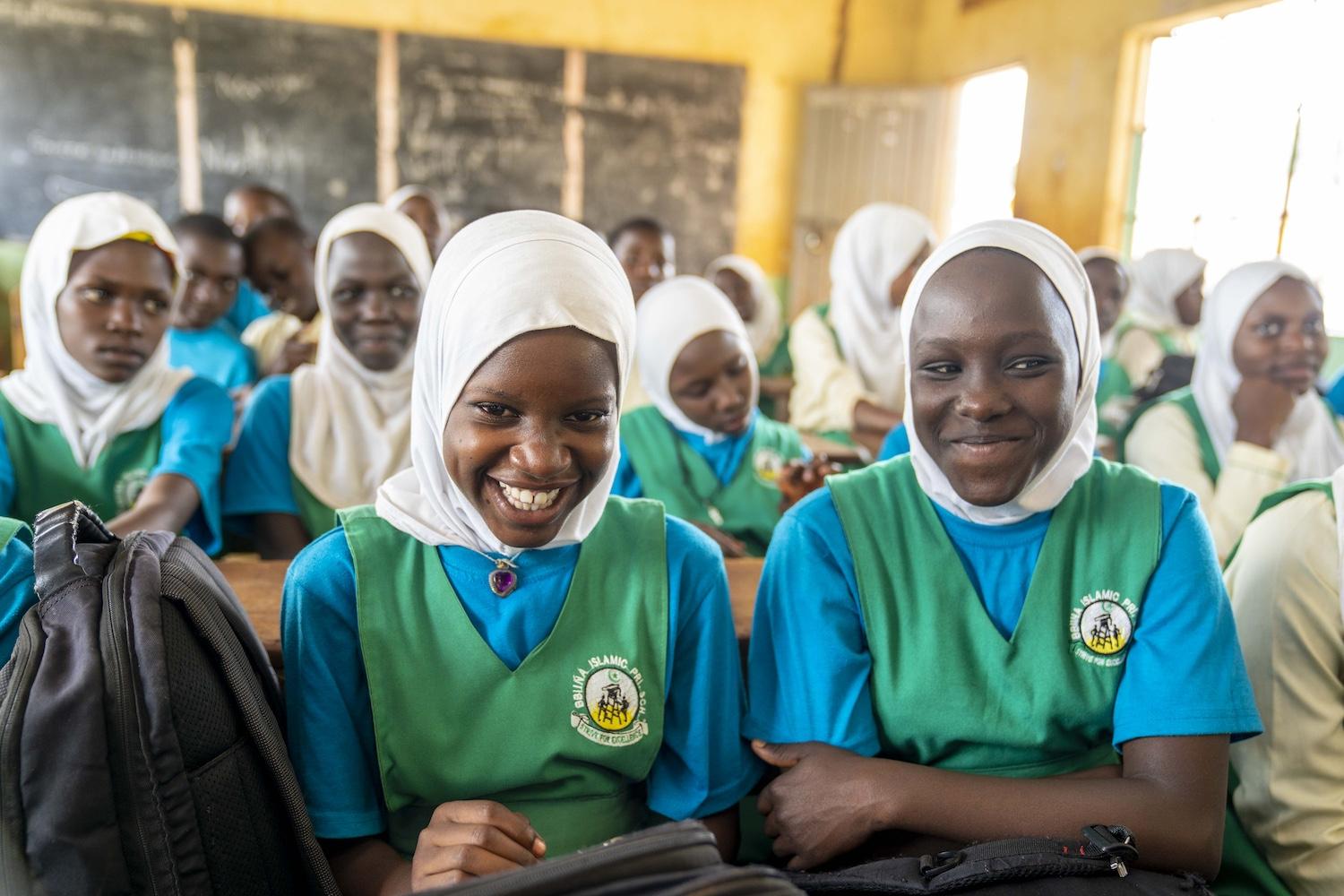 Two girls participating in Girls Up Initiative Uganda programming at their school smile at the camera.