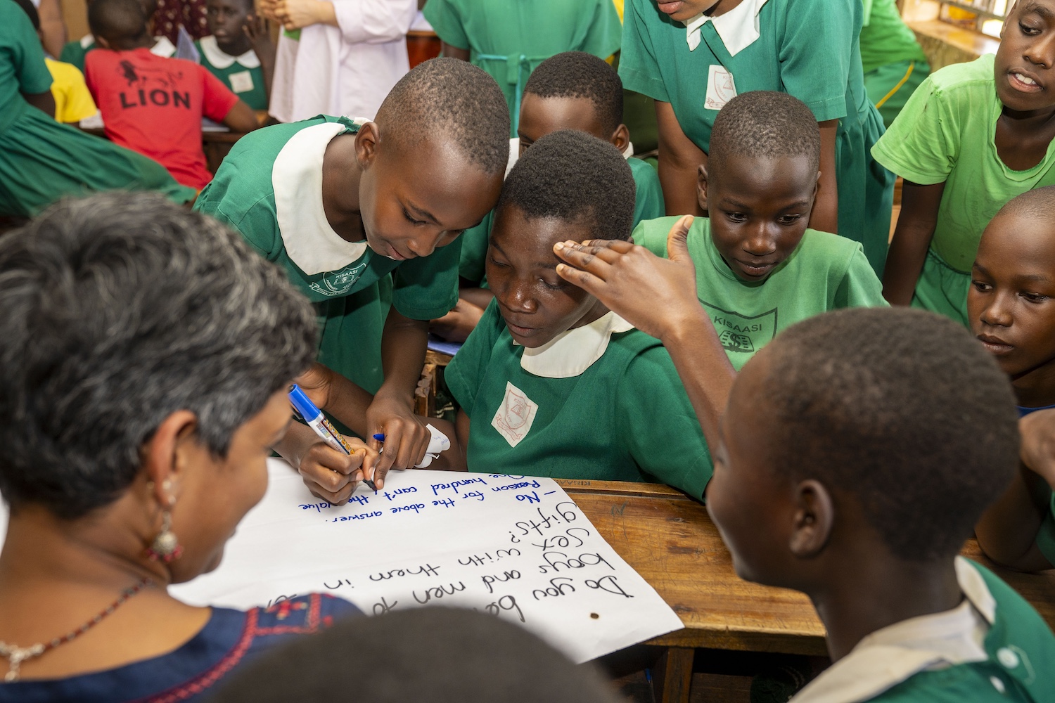 Boys participate in Girl Up Initiative Uganda programming at their school, writing their responses to a question on a large piece of paper in a group