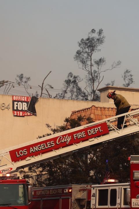 A firefighter climbs a fire truck ladder while responding to the Palisades Fire — LA wildfires