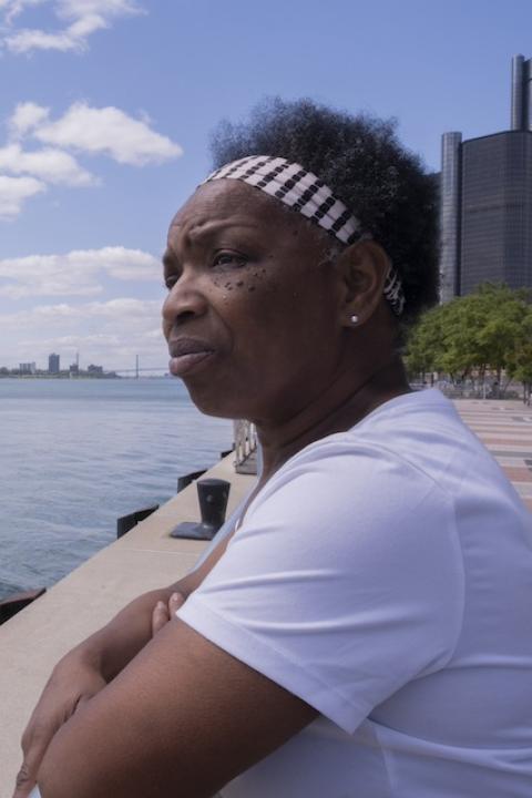 Sandra Turner-Handy overlooks a body of water with the Detroit skyline behind her — industrial air pollution