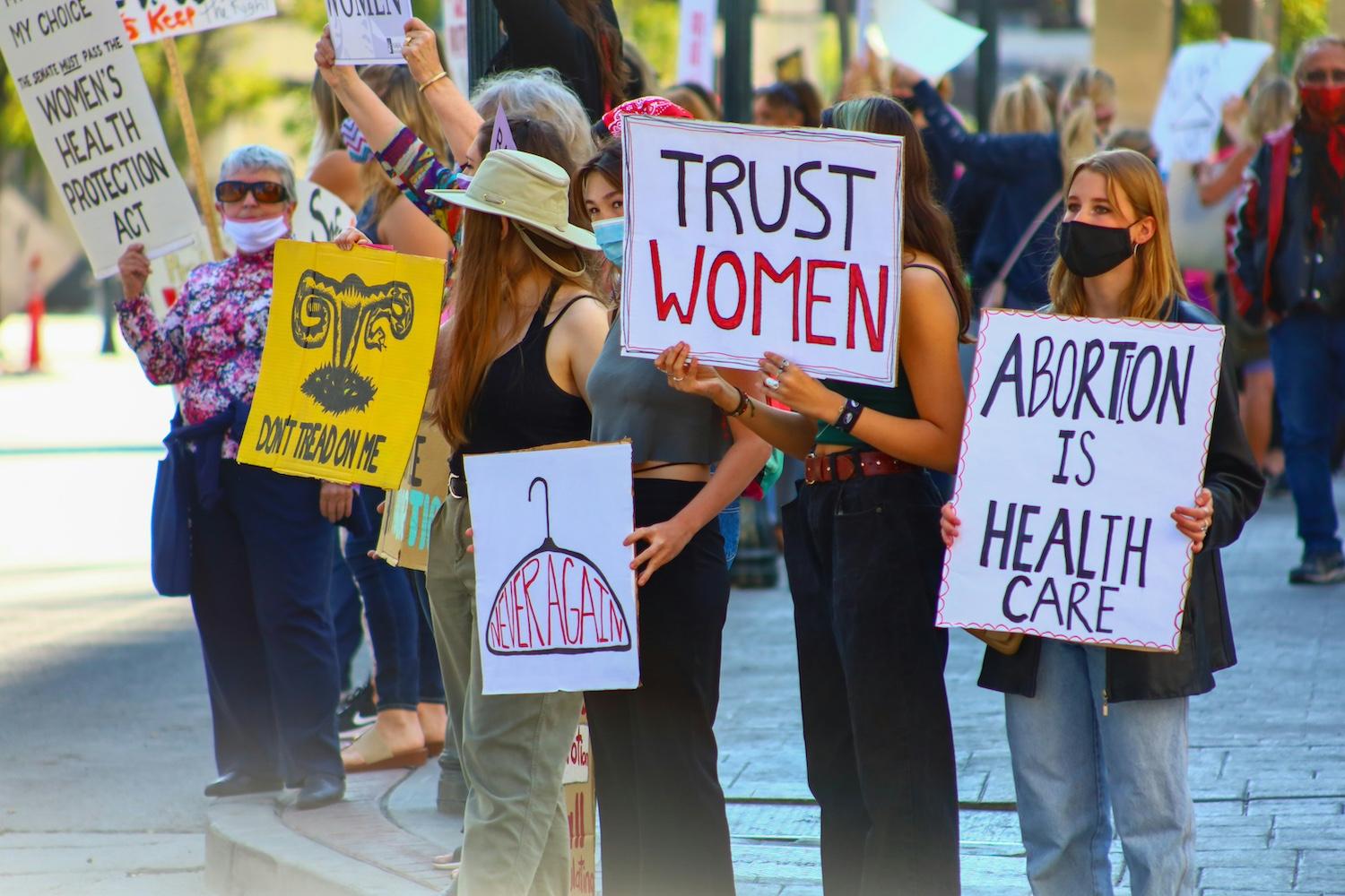 Protesters hold signs that read "Trust women" and "Abortion is health care" — maternal health