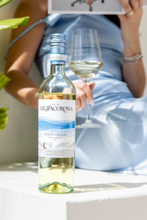 A woman sips Mezzacorona wine out of a glass while sitting next to the bottle — sustainable wine