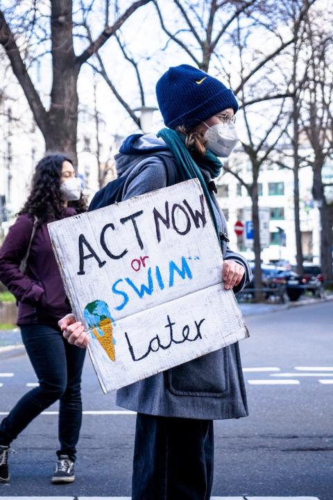 A climate activist holds a sign that states "act now or swim later."