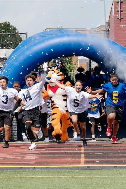 Students run onto a football field with Tony the Tiger as part of Mission Tiger.