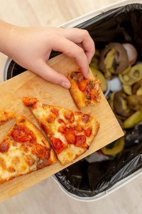 person discarding pizza and leftover food in the trash — reducing methane from food waste as a climate solution