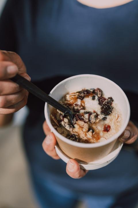 person eating oatmeal and fruit out of a takeout cup