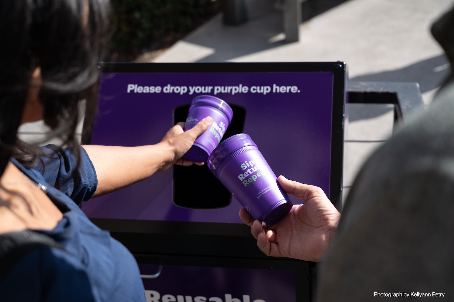 Two people return purple reusable cups at a drop-off bin for thePetaluma Reusable Cup Project.