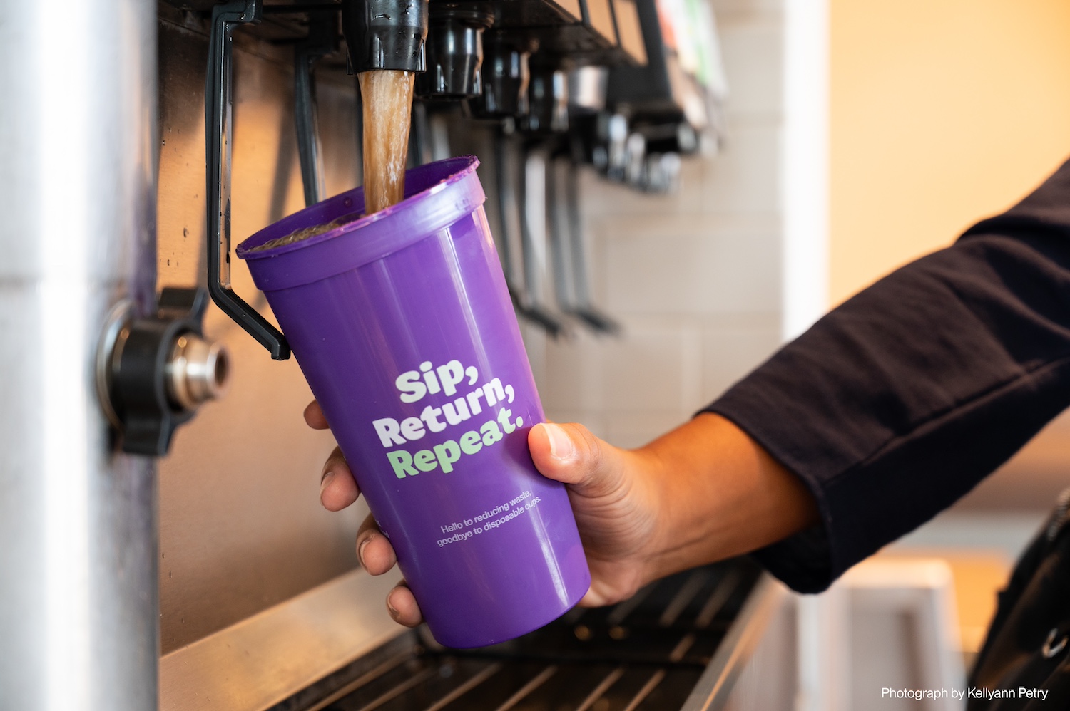A person fills up a purple Petaluma Reusable Cup Project cup at a soda fountain.