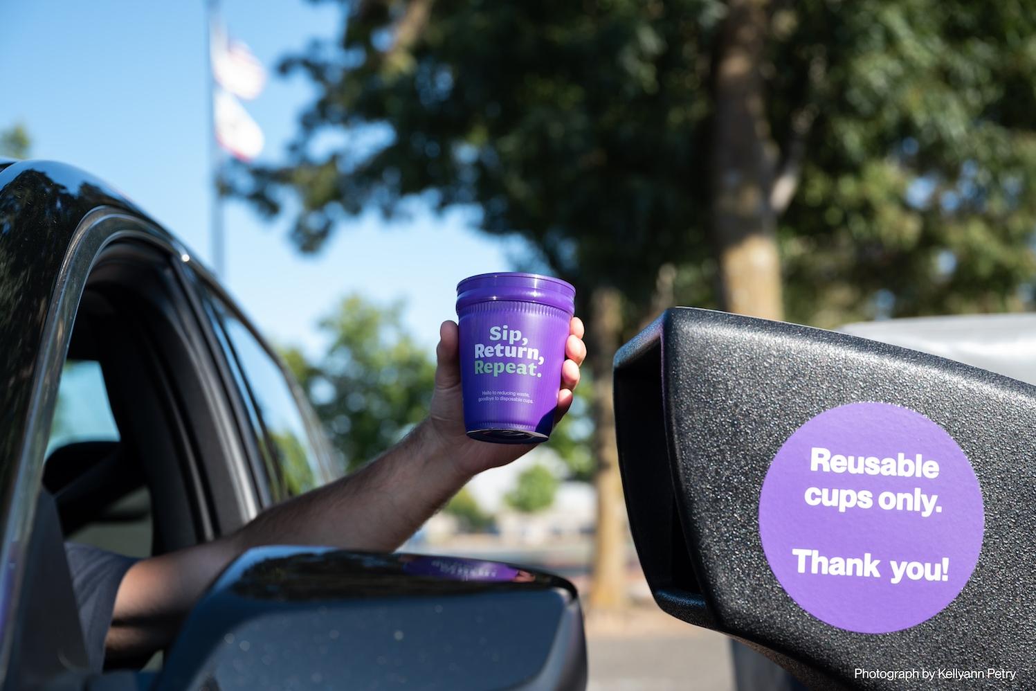 A person uses a drive-up drop off bin to return their purple, reusable cup as a part of the Petaluma Reusable Cup Project.