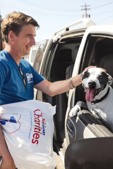 A PetSmart Charities volunteer petting a dog in car and holding a bag of dog food — food insecurity