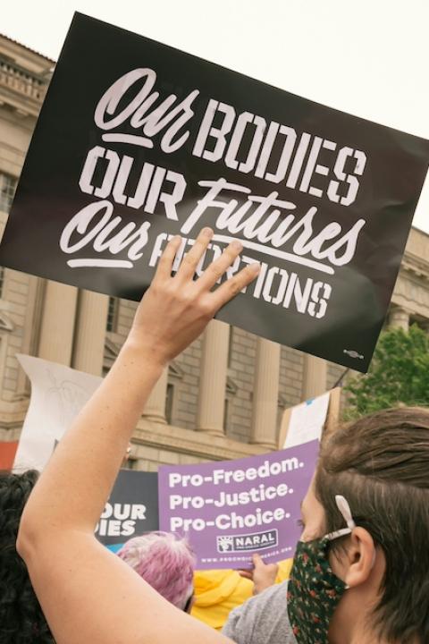 An attendee of a reproductive rights protest holds a sign that reads "Our bodies, our futures, our abortions."