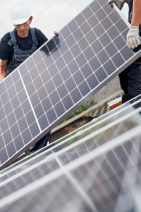 Two people installing solar panels on a roof.