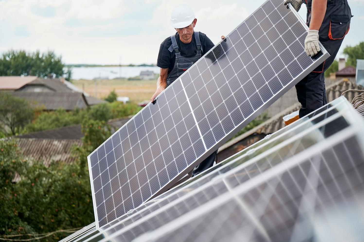 Two people installing solar panels on a roof.