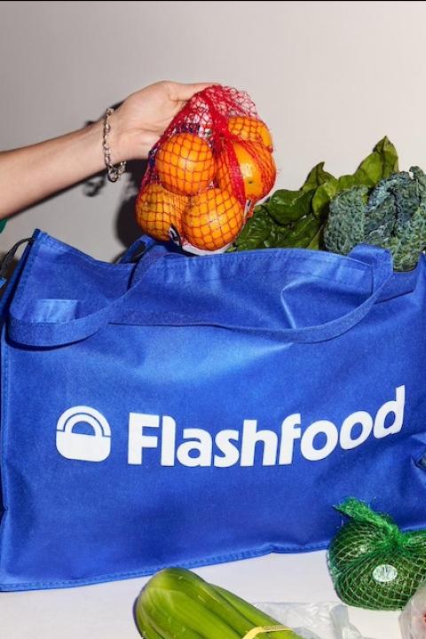 A person pulls a bag of oranges out of a reusable Flashfood bag — solutions journalism