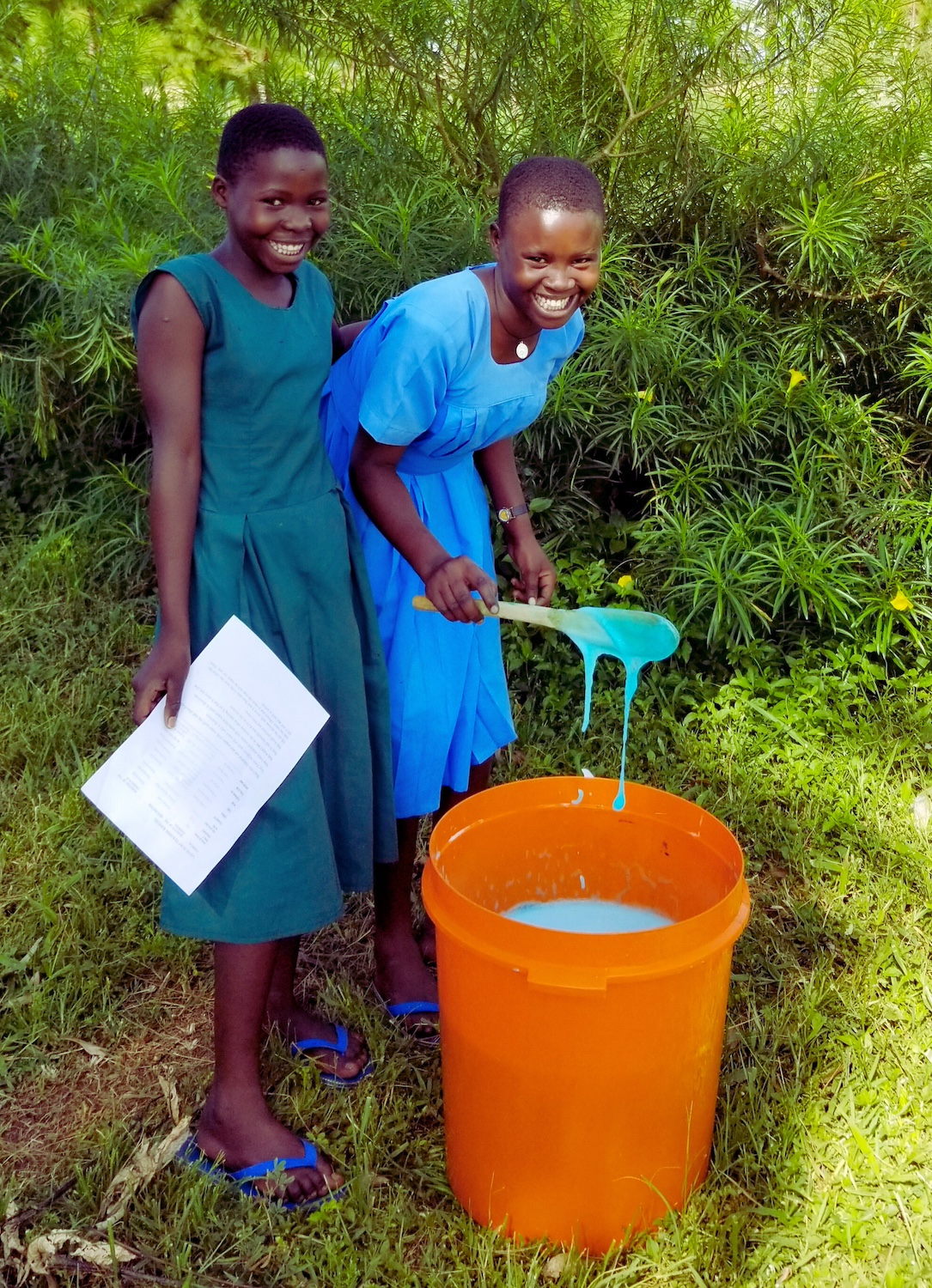 Two girls make blue soap in a bucket during a Surge for Water soapmaking lesson.