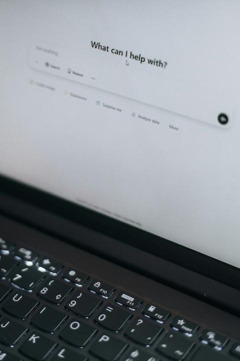 An open laptop displays the ChatGPT homepage, which reads, "What can I help with?" — AI