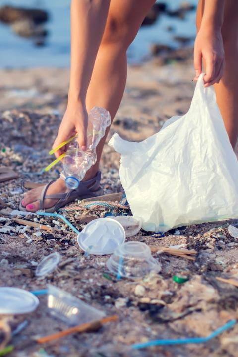 woman picks up plastic pollution from a beach