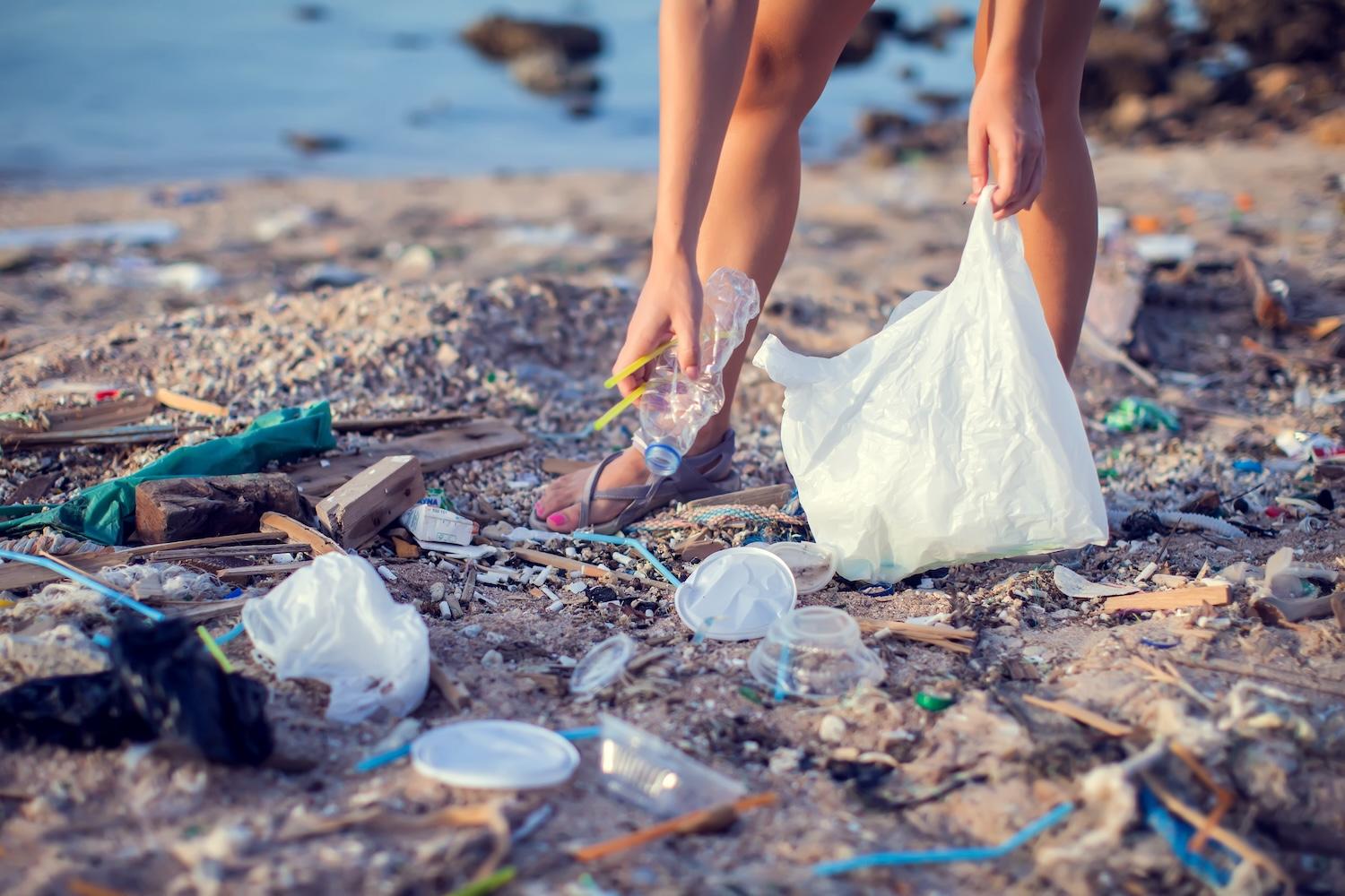 woman picks up plastic pollution from a beach