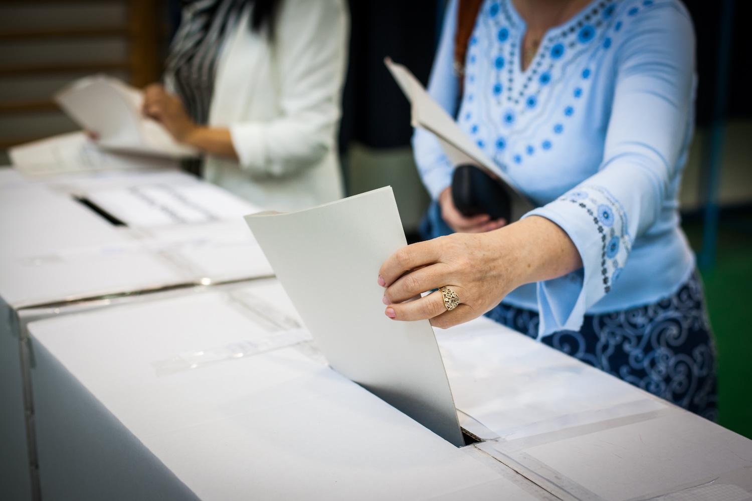 woman puts ballot in a ballot box — voting — paid time off for voting