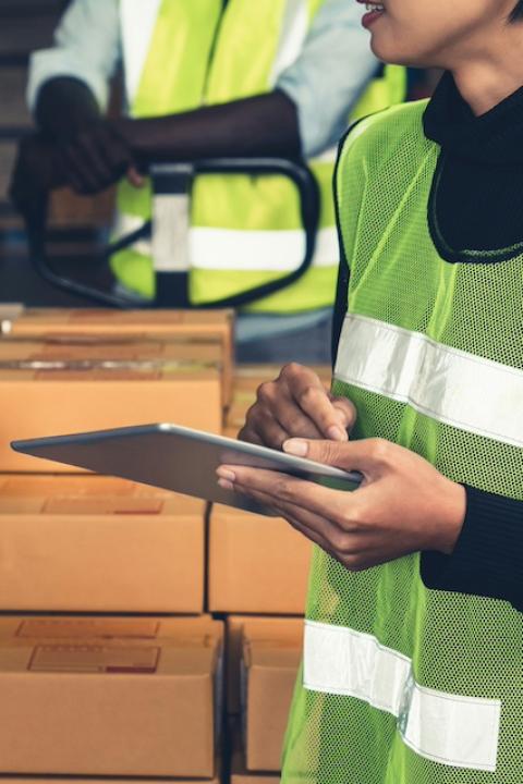 A supply chain worker holding a tablet talks with other workers in a warehouse — worker voice