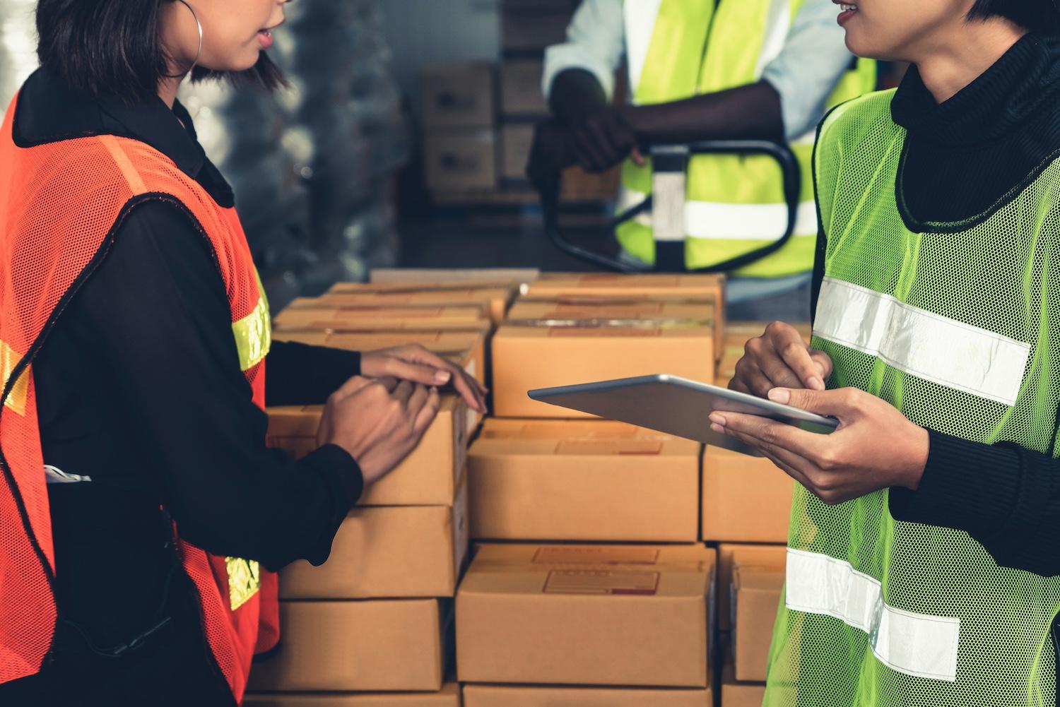 A supply chain worker holding a tablet talks with other workers in a warehouse — worker voice