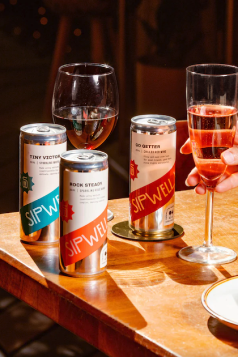 Three cans of wine from Sipwell Wine Co. sit on a table alongside glasses of the wine — sustainable wine